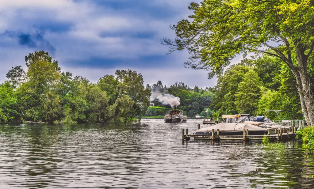 Ein nostalgisches Dampfschiff fährt durch den malerischen Silkeborg See in Dänemark, umgeben von üppigen, grünen Bäumen und ruhigem Wasser