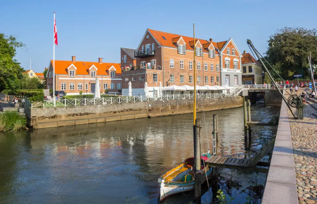 Szenische Hafenszene in Ribe, Dänemark, mit traditionellen Gebäuden und Booten am Wasser bei klarem Himmel.