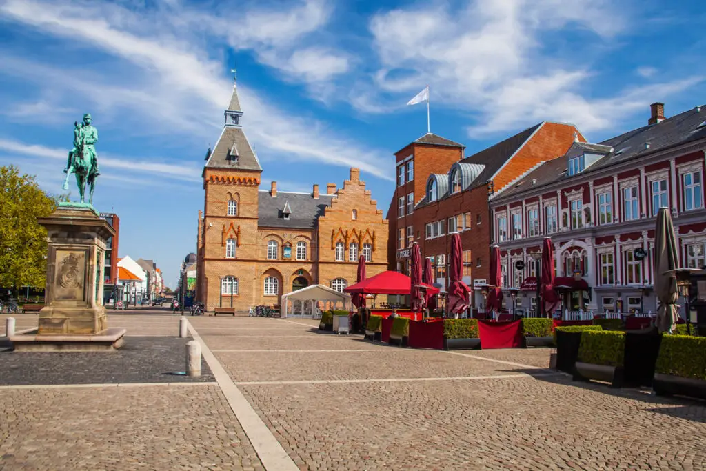 Weitläufiger Marktplatz in Esbjerg, Dänemark, mit historischen Gebäuden und einem Reiterstandbild unter blauem Himmel.