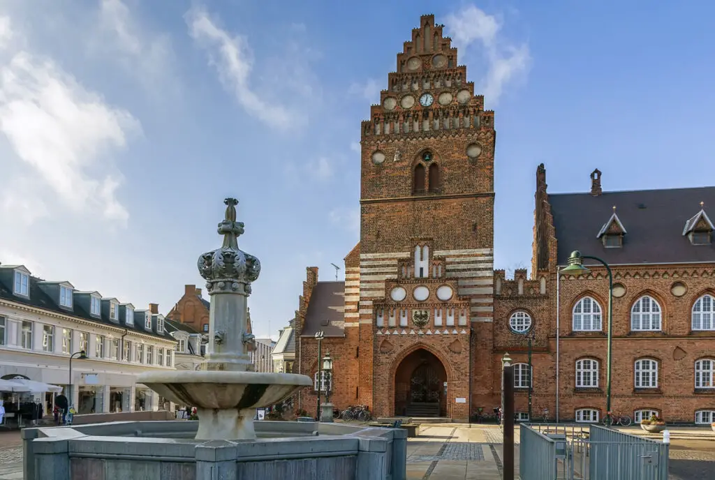 Das imposante Rathaus von Roskilde, Dänemark, mit seinem markanten, historischen Ziegelturm und einem Brunnen im Vordergrund.