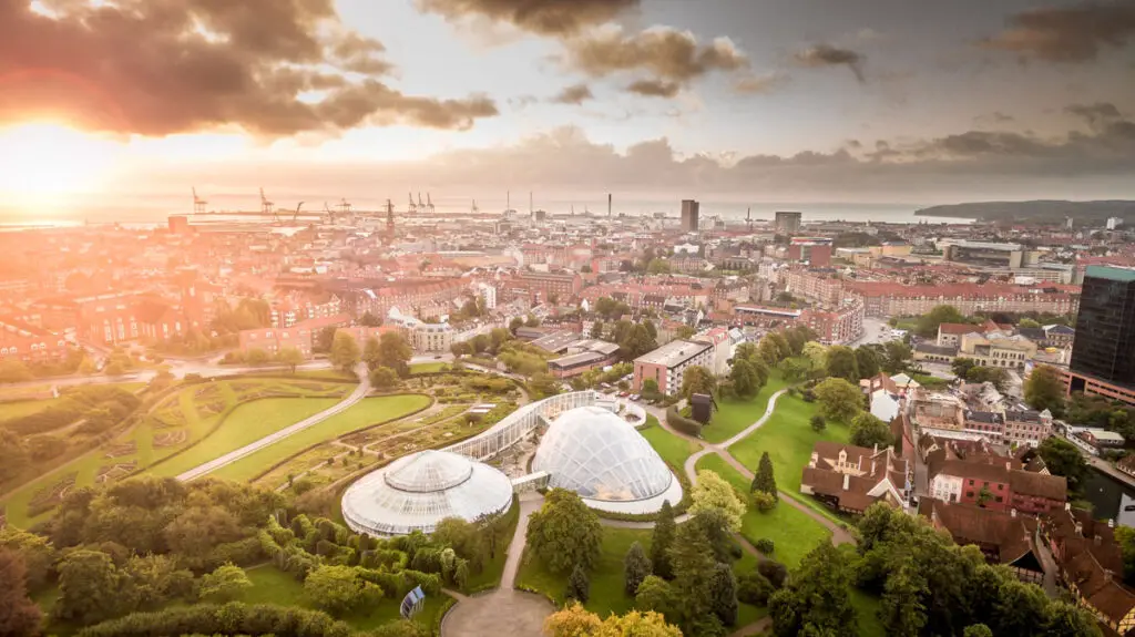 Weitläufiger Blick über die Stadt Aarhus, Dänemark, bei Sonnenuntergang, mit modernen und historischen Gebäuden sowie üppigen Parks.