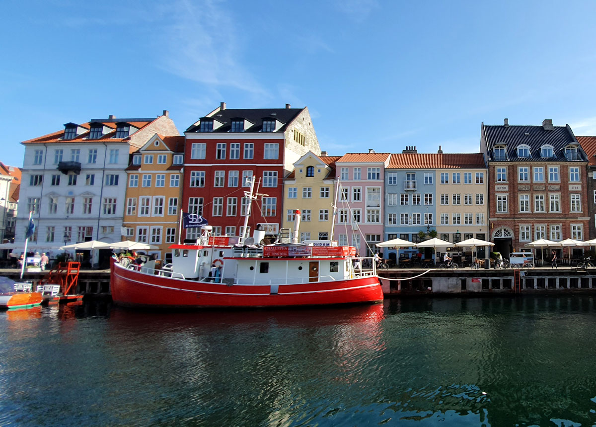Bunte Häuserfronten am Nyhavn-Kanal in Kopenhagen, Dänemark, mit einem roten Boot im Vordergrund unter klarem, blauem Himmel.