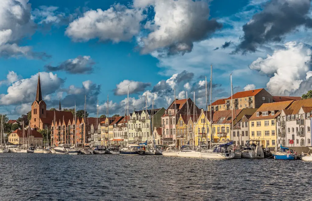 Panoramablick auf den Hafen von Sønderborg, Dänemark, mit farbenfrohen Gebäuden und Segelbooten unter einem bewölkten Himmel.